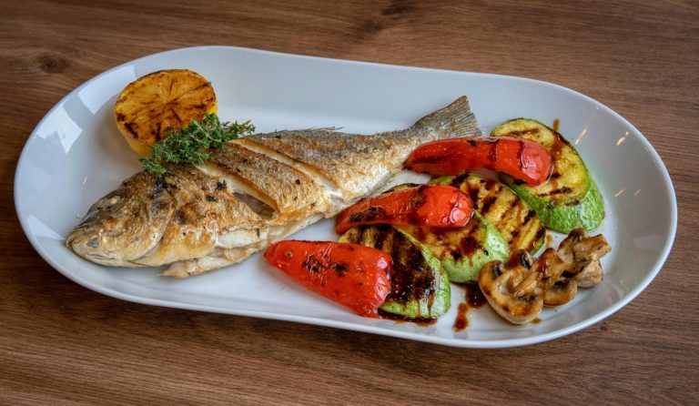 Mittagstisch Freitag, 12.06.2026 4 Grilled fish served with roasted vegetables on a ceramic plate.