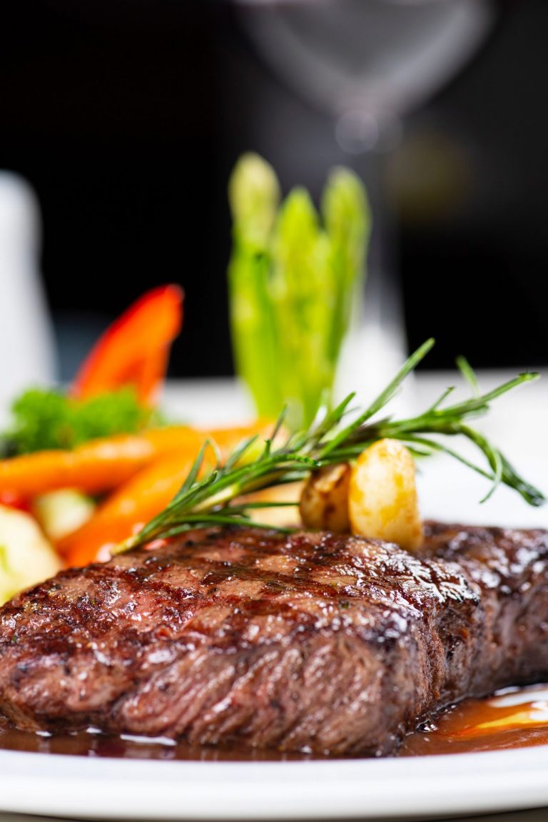 Close-up of a juicy grilled steak with colorful vegetables on a plate, perfect for a gourmet meal.