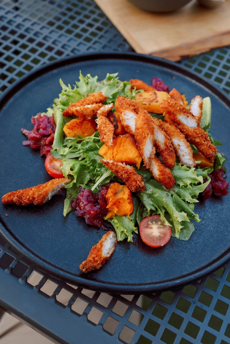 Delicious crispy chicken salad with greens, tomatoes, and veggies on a black plate.