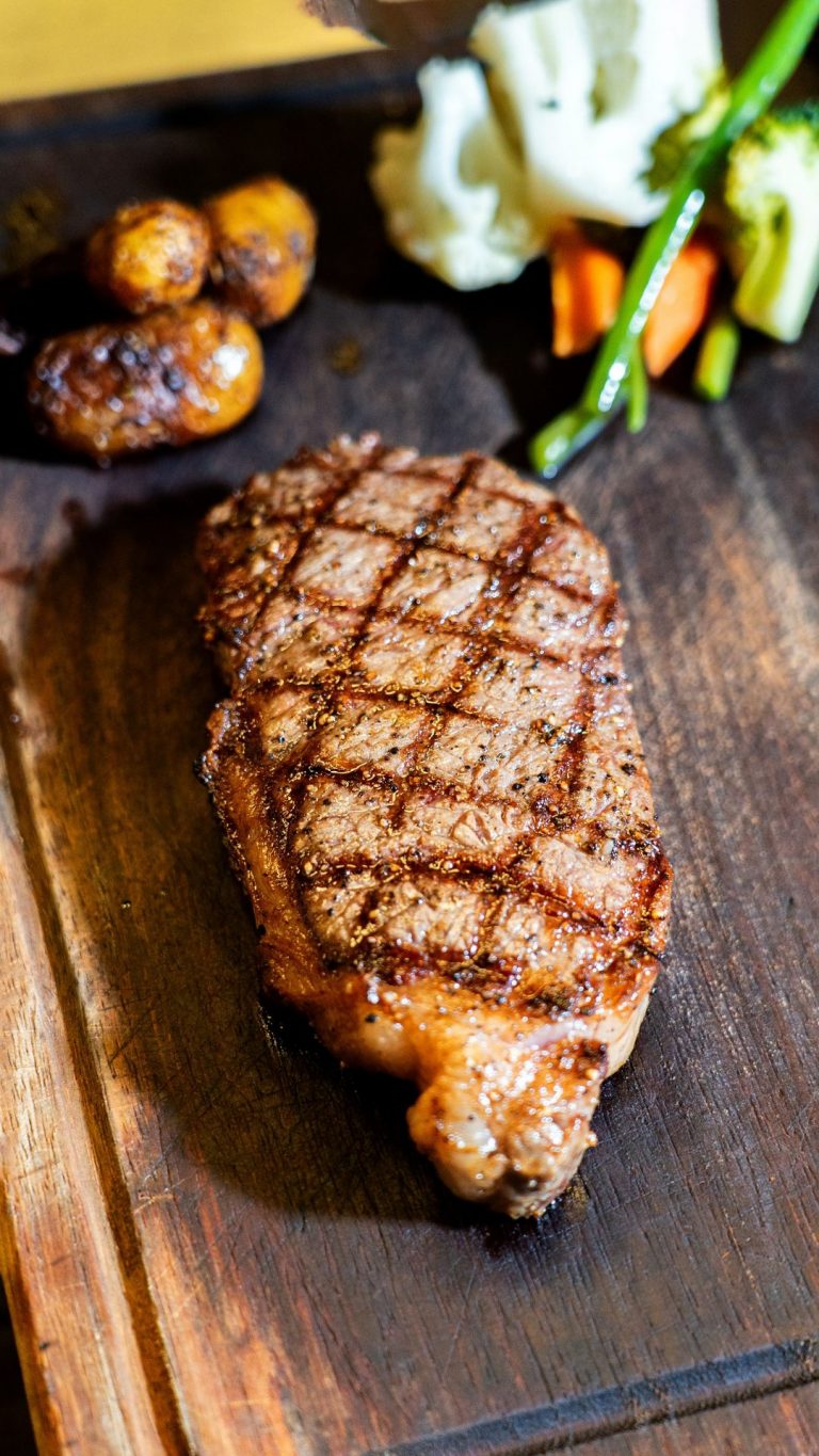 Juicy grilled steak served with assorted roasted vegetables on a rustic wooden board.